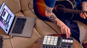 An acoustic guitarist sat on their sofa with a laptop running Guitar Rig 7 Player next to them