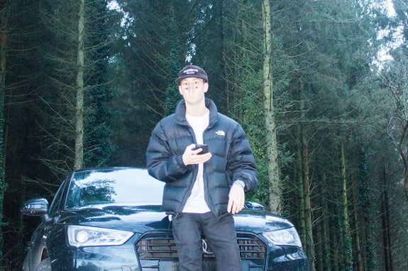 George Cotton AKA Grace posing against a forest background while leaning on an Audi
